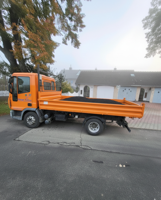 Lkw von Maage Bau liefert Schotter zur Baustelle in Wesertal, mit orangefarbener Ladefläche und Wohngebäuden im Hintergrund.